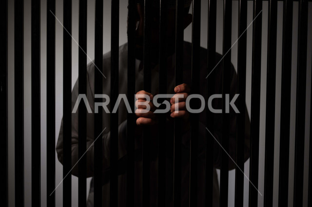 رجل عربي خليجي سعودي داخل السجن ، يمسك القضبان الحديدية ، سجين سعودي ينتظر الحرية ، الشعور بالندم والوحدة 