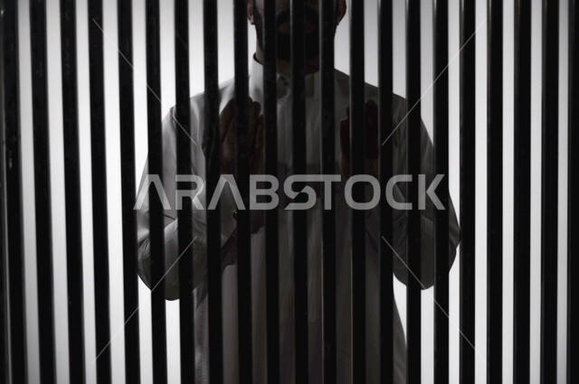 رجل عربي خليجي سعودي خلف قضبان السجن ، يرفع يديه لاعلى يناجي الله، الدعاء والتوبة لله ، صلاة وعبادة