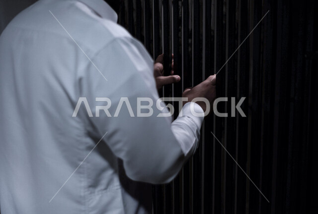 رجل عربي خليجي سعودي داخل السجن ، يمسك القضبان الحديدية ، سجين سعودي ينتظر الحرية ، الشعور بالندم والوحدة 