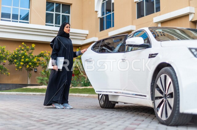 A veiled Saudi Arabian Gulf businesswoman, holding a mobile device in her hand, opens the back door of the car, preparing to board the car, passenger delivery service, comfort and safety
