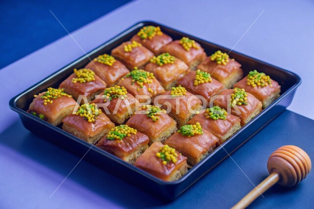 حلويات لذيذة بالفستق والمكسرات، ضيافة الأعياد والمناسبات في المملكة العربية السعودية، أكلات غنية بالسكريات والسعرات الحرارية، وصفات الأطعمة العربية الشرقية، طبق معدني مليئ بقطع البقلاوة الشهية على الطريقة التقليدية، خلفية زرقاء