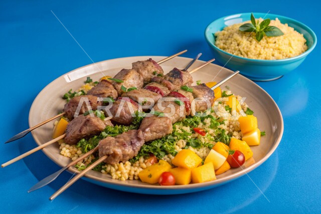 قطع لحم الضأن المشوية المرتبة على طبق مع سلطة الكسكس الشهية، وصفات وأطباق المتميزة، مطاعم للمأكولات الشرقية في المملكة العربية السعودية، وجبات اللحم الصحية والمغذية، خلفية زرقاء
