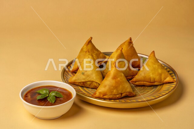 أطباق رئيسية في سفرة إفطار شهر رمضان المبارك، فطائر مقلية متنوعة الحشوات، مقبلات رمضانية شهية، وصفات المأكولات والأطعمة العربية الشرقية السعودية اللذيذة ، طبق من السمبوسك المقرمشة مع صلصة التمر هندي، خلفية صفراء