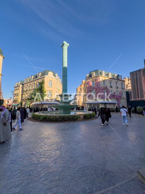 Enjoying enjoyable experiences in the most prominent entertainment areas in the Kingdom of Saudi Arabia, tourist attractions, the French Village on Boulevard World in the city of Riyadh, modern architectural art, a picture of a water pond decorated with herbs in the middle of the square.