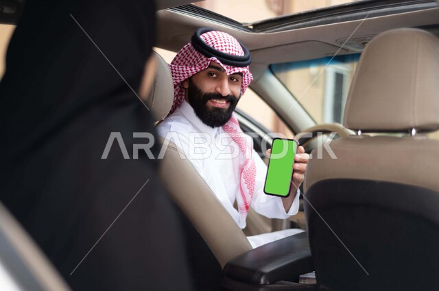 سائق عربي خليجي سعودي يقود السيارة ، يحمل بيده الهاتف المحمول ، امرأة عربية خليجية سعودية محجبة ، تستقل سيارة اجرة ، خدمة النقل من خلال تطبيق التوصيل، تحديد الموقع  ، خدمة توصيل الركاب ، راحة وامان