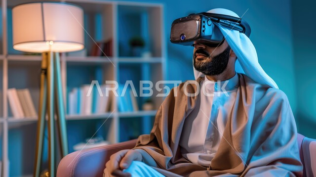 لعب ألعاب الفيديو ثلاثية الأبعاد، الأجهزة والتقنيات الحديثة والمتطورة، محاكاة العالم الخيالي، تعابير التركيز والاندماج، صورة مقربة لرجل عربي خليجي سعودي يرتدي الثوب التقليدي والشماغ يجلس على اريكة مريحة يقوم بمشاهدة الأفلام عبر نظارة الواقع الإفتراضي