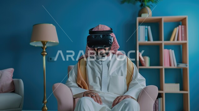 محاكاة العالم الخيالي، تعابير التركيز والاندماج، صورة مقربة لرجل عربي خليجي سعودي يرتدي الثوب التقليدي والشماغ يجلس على اريكة مريحة يقوم بمشاهدة الأفلام عبر نظارة الواقع الإفتراضي، الأجهزة والتقنيات الحديثة والمتطورة، لعب ألعاب الفيديو ثلاثية الأبعاد