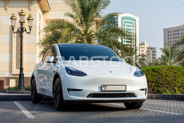 موديلات السيارات  الحديثة المتطورة، سيارة تسلا الكهربائية مركونة في الشارع أمام المسجد باللون الابيض في مدينة الشارقة بالإمارات العربية، الحد من انبعاث ثاني أكسيد الكربون، المحافظة على البيئة، استعمال الطاقة النظيفة، التقدم التقني والكنولوجي