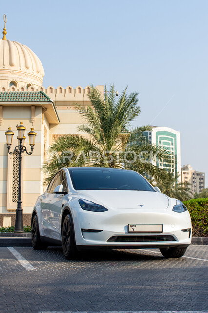 Modern advanced car models, Tesla electric car parked on the street in front of the mosque in white in Sharjah city in the United Arab Emirates, reducing carbon dioxide emissions, preserving the environment, using clean energy, technical and technological progress