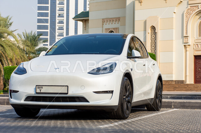 موديلات السيارات  الحديثة المتطورة، سيارة تسلا الكهربائية مركونة في الشارع أمام المسجد باللون الابيض في مدينة الشارقة بالإمارات العربية، الحد من انبعاث ثاني أكسيد الكربون، المحافظة على البيئة، استعمال الطاقة النظيفة، التقدم التقني والكنولوجي