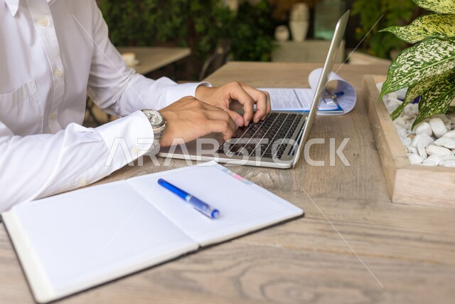 استخدام الاجهزة التقنية الحديثة، ادارة مهام العمل اليومية في مقر الشركة، صورة مقربة لرجل عربي خليجي سعودي يرتدي الزي التقليدي يجلس في مكتبه يعمل على جهاز الحاسوب المحمول، مهن ووظائف سعودية