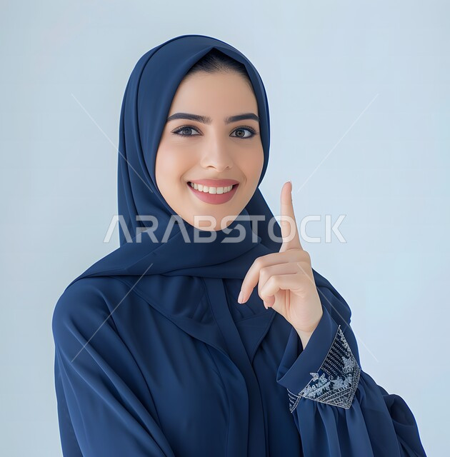  إيماءات وجه تدل على الفرح و السرور، بورتريه لمرأة عربية خليجية سعودية محجبة ترتدي العباءة  تشير بإصبع السبابة للاعلى،  تقوم بإيماءات يد مختلفة، خلفية زرقاء
