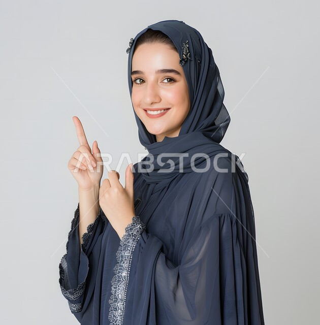  إيماءات وجه تدل على الفرح و السرور، بورتريه لمرأة عربية خليجية سعودية محجبة ترتدي العباءة  تشير بإصبع السبابة للاعلى،  تقوم بإيماءات يد مختلفة، خلفية رمادي