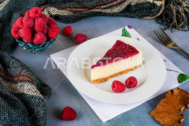 A piece of cheesecake decorated with blueberries and a layer of red sauce, delicious cold desserts, sweets and high-calorie foods, falling leaves and a scarf for the shoulders indicate a beautiful autumn atmosphere