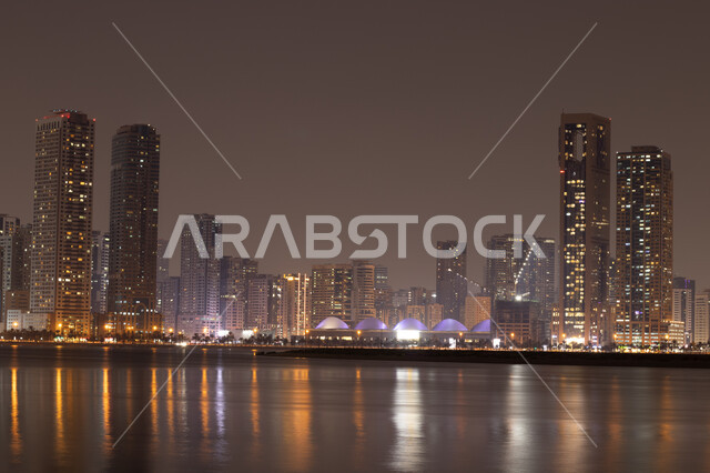 المباني والمنشآت والأبراج المضيئة ليلا المطلة على الخليج العربي، استقطاب وجذب السياح الى الأماكن السياحية المشهورة، كورنيش بحيرة الخان في مدينة الشارقة بالامارات العربية المتحدة، اطلالة على وجهة المجاز البحرية