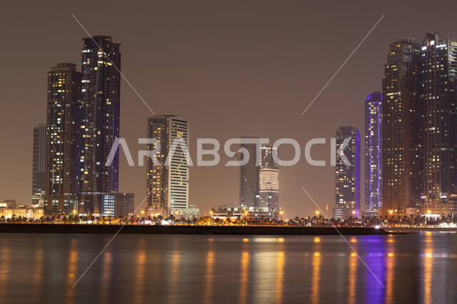 الأبراج وناطحات السحاب المضيئة ليلا المطلة على الخليج العربي، استقطاب وجذب السياح الى الأماكن السياحية المشهورة، كورنيش بحيرة الخان في مدينة الشارقة بالامارات العربية المتحدة، اطلالة على وجهة المجاز البحرية