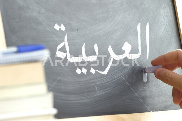 Developing students' linguistic and intellectual abilities, fun Arabic language class, teaching students to form words, close-up image of a hand holding chalk and writing the word Arabic on the blackboard, schools in the Kingdom of Saudi Arabia