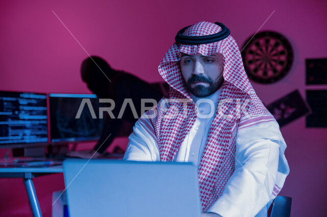 Saudi Arabian Gulf man using laptop, masked man using computer screens, committing illegal acts, cyber espionage, cyber attack, data theft, cyber security