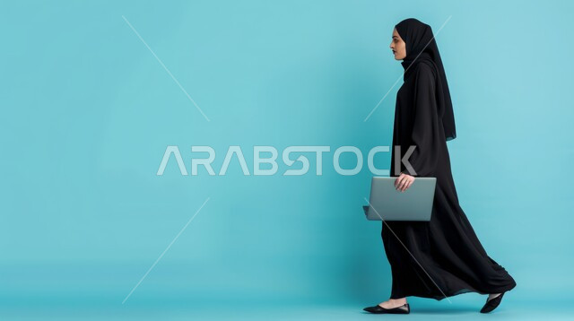 The concept of self-confidence, a side portrait of a veiled Saudi Arabian Gulf woman wearing a black abaya, holding a laptop, use of modern and advanced technological devices, walking and moving forward gestures, full-length body, blue background.