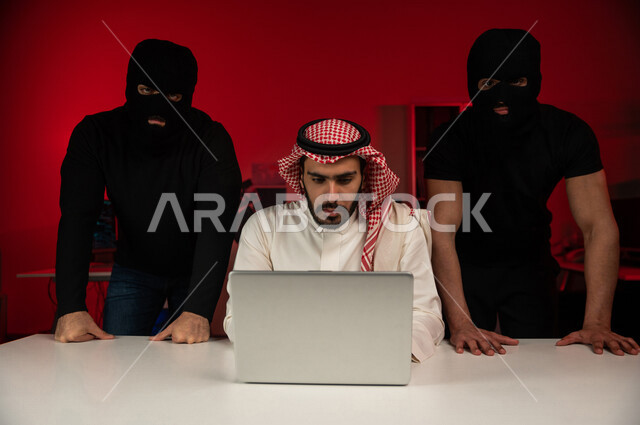 A Saudi Arabian Gulf man and two masked men in front of a laptop, planning fraud, cyber espionage, cyber attack, cyber crimes, cyber security