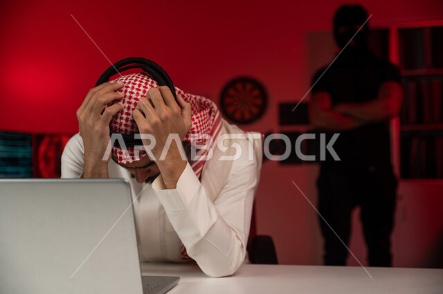 A Saudi Arabian Gulf man sitting in front of a laptop, masked men standing behind, a Saudi man exposed to loss and fraud, exposure to electronic attack, personal data theft, electronic crimes, cyber security