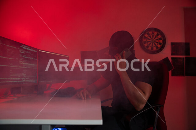 Masked man using mobile phone, sitting in front of computer screens, cyber espionage, cyber attack, data theft via the Internet, cyber crime, cyber security