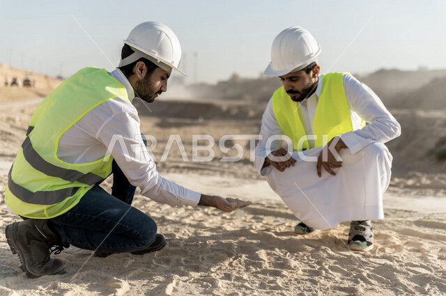 مقاول ومشرف العمل يرتديان خوذة وسترة خاصة بالعمل، عربيان خليجيان سعوديان يقومان باختبار جودة الرمل بموقع العمل  ، التحقق من وجود الطين الزائد ،اشراف ومتابعة العمل ، متابعة استراتيجية المشروع