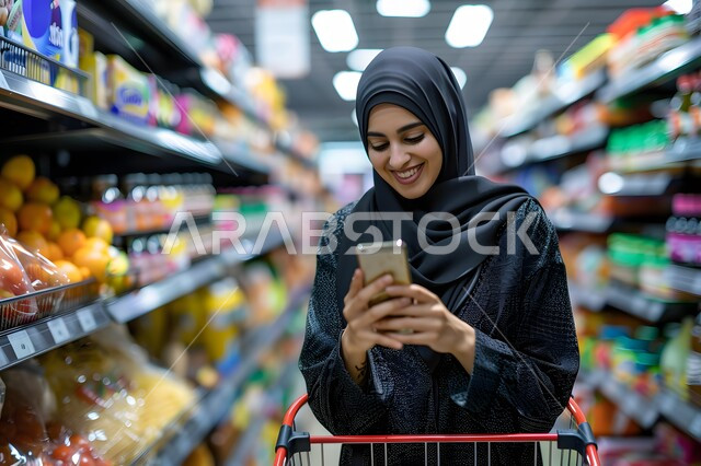 الاستمتاع بالتسوق والشراء من المول, بورتريه امرأة عربية خليجية سعودية مبتسمة محجبة ترتدي  العباءة السوداء تنظر إلى الهاتف المحمول بإيماءات الفرح والسرور, الاستفادة من العروض والتخفيضات.