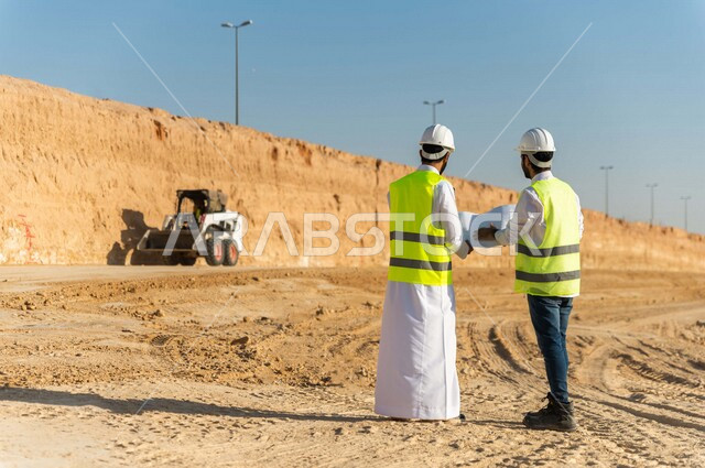 مقاول ومشرف العمل يرتديان خوذة وسترة خاصة بالعمل، عربيان خليجيان سعوديان يناقشان ورقة مخطط البناء ،اشراف ومتابعة العمل ، متابعة استراتيجية المشروع ، التصاميم المعمارية والانشائية