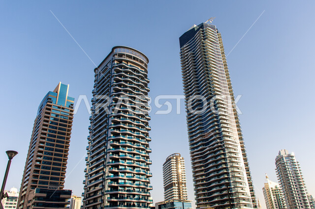 الهندسة الفنية المعمارية على الطراز الحديث للمباني وناطحات السحاب, الأبراج المطلة على مرسى اليخوت في مارينا دبي على ساحل الخليج العربي, معالم سياحية مشهورة وقت النهار, الإهتمام بتشجير الأشجار والنباتات الخضراء في الامارات العربية المتحدة