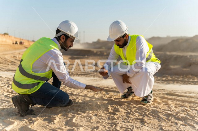 مقاول ومشرف العمل يرتديان خوذة وسترة خاصة بالعمل، عربيان خليجيان سعوديان يقومان باختبار جودة الرمل بموقع العمل  ، التحقق من وجود الطين الزائد ،اشراف ومتابعة العمل ، متابعة استراتيجية المشروع
