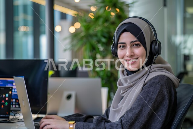 الجلوس وراء المكتب وتنفيذ الأعمال على جهاز الحاسوب, تمكين عمل المرأة في المجتمع السعودي, شابة عربية خليجية سعودية محجبة ترتدي زي الكاجوال وتنظر للكاميرا بإيماءات السرور, مهن ووظائف نسائية سعودية, التوظيف في مجال خدمة العملاء والرد على الاسئلة والاستفسارات