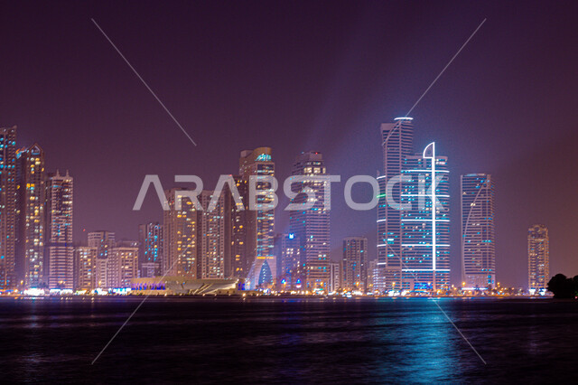 الفن الهندسي المعماري للأبراج وناطحات السحاب المضيئة ليلا المطلة على الخليج العربي، المعالم السياحية المشهورة، اماكن جذب واستقطاب السياح، اطلالة على الوجهة البحرية، كورنيش بحيرة خالد في مدينة الشارقة بالامارات العربية المتحدة
