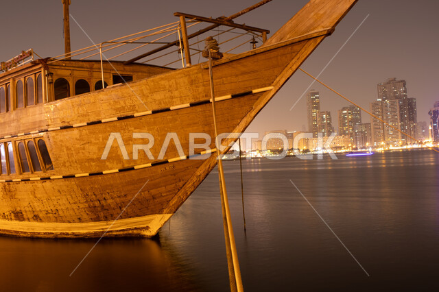 Architectural art of illuminated towers and skyscrapers at night, view of the seafront, famous tourist attractions, tourist attractions, view of the Corniche in Sharjah city in the United Arab Emirates, a wooden ship sailing in the Arabian Gulf
