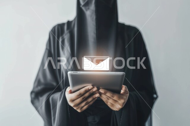 Technological progress in Saudi Arabia, technological and digital development, close-up portrait of a veiled Saudi Arabian Gulf woman wearing a black abaya holding a tablet in her hands, holographic icon for email notification, gray background