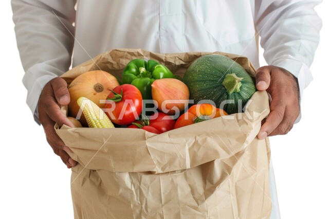 مفهوم النظام الغذائي الصحي, الالتزام بأكل المأكولات الصحية, بورتريه مقرب لرجل عربي خليجي سعودي يرتدي الثوب التقليدي يحمل بيديه كيس من الخضراوات الطازجة, خلفية بيضاء