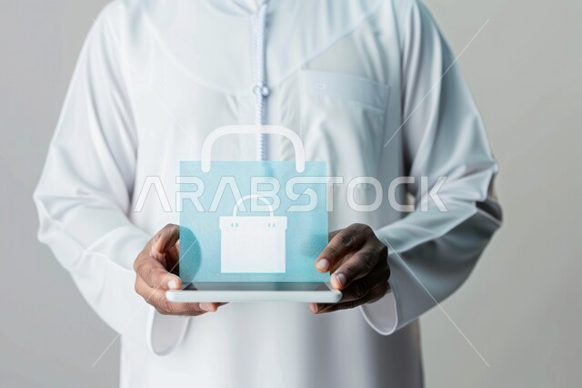 E-shopping concept, remote purchasing and payment, technical development in Saudi Arabia, close-up portrait of a Saudi Arabian Gulf man wearing traditional thobe holding a tablet with a holographic shopping bag icon, gray background