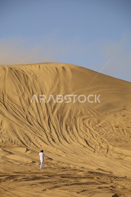 فعاليات ترفيهية تجذب السياح، مشجع عربي خليجي سعودي يرتدي الثوب التقليدي ويقف ليشاهد عروض ركوب السيارة على الكثبان والتلال الرملية، القيام بمغامرات بواسطة مركبة الدفع الرباعي في صحاري المملكة, هواية التطعيس بالسيارات, قيادة المركبات في صحراء ناوان بمنطقة الباحة
