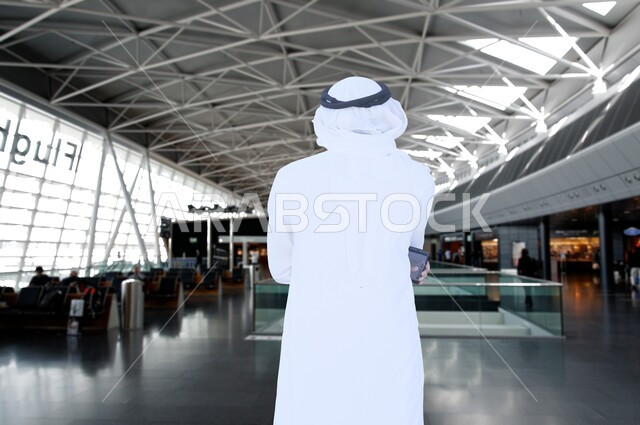  الاستعداد للسياحة والسفر، صورة من الخلف لرجل عربي خليجي اماراتي يرتدي الكندورة والثوب الابيض يقف باستقامة يحاول التفكير بشيء ما، الفن الهندسي المعماري في المطار، أهمية السياحة في دول الخليج