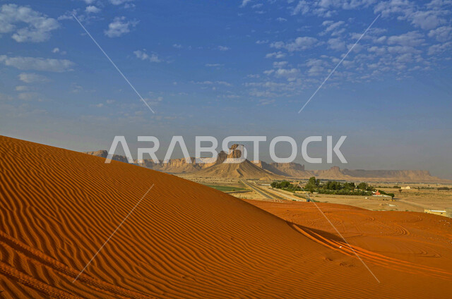 البيئة الطبيعية الخليجية الجافة، تشكل الكثبان والقمم الرملية في الصحاري, المساحات الصحراوية الشاسعة الممتدة على طول الأفق, مشهد لتداخل ألوان رمال الصحراء الذهبية اللامعة مع خلفية السماء الزرقاء الملبدة بالغيوم 
