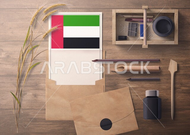 ورقة بيضاء تحمل العلم الاماراتي، تصميم هوية تجارية تتعلق بدولة الامارات، صورة من الاعلى لمجموعة من الادوات المكتبية والاكسسوارات على سطح خشبي، مفهوم رسالة الاحتفال