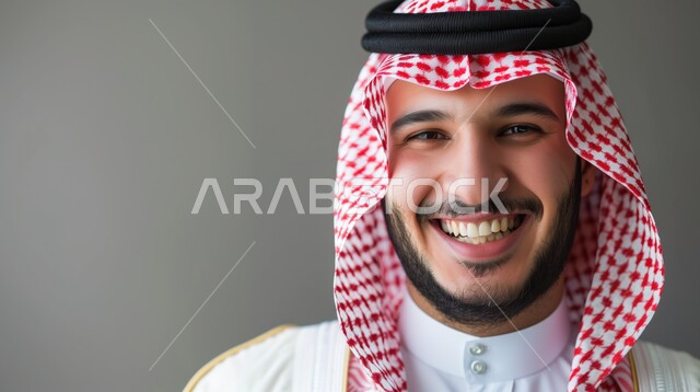 الاهتمام بالأناقة والمظهر الخارجي، بورتريه مقرب لرجل عربي خليجي سعودي مبتسم يرتدي الشماغ والثوب التقليدي ينظر إلى الكاميرا بإيماءات السرور، الشعور بالثقة في النفس، صورة شخصية للوثائق الرسمية، خلفية رمادية