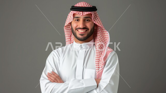 الاهتمام بالأناقة والمظهر الخارجي، بورتريه مقرب لرجل عربي خليجي سعودي مبتسم يرتدي الشماغ والثوب التقليدي ينظر إلى الكاميرا بإيماءات السرور، الشعور بالثقة في النفس، صورة شخصية للوثائق الرسمية، خلفية رمادية