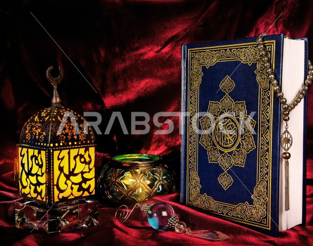إضاءة وزينة شهر رمضان المبارك، مصابيح وأنوار في الأجواء الرمضانية الروحانية، تحف و اكسسوارات تقليدية للاحتفال بقدوم شهر الخير، فانوس عربي معدني مزخرف على طاولة خشبية مع المصحف الشريف والمسبحة