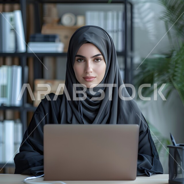 إنجاز المهام المطلوبة عبر الحاسوب المحمول، وظائف ومهن مكتبية سعودية، دمج العمل مع التكنولوجيا، إدارة شؤون الشركة وتنظيمها عبر الاجهزة التقنية، صورة مقربة لامرأة عربية خليجية سعودية محجبة تعمل في المكتب