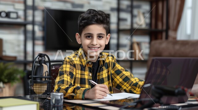 طالب يجلس على طاولة الدارسة ويمسك بيده القلم ويضع الدفتر امامه, الاجتهاد والمشاركة التطوعية من خلال دورات التعلم عن بعد، بورتريه لتلميذ عربي خليجي سعودي, يحضر دروسه عن طريق الكمبيوتر