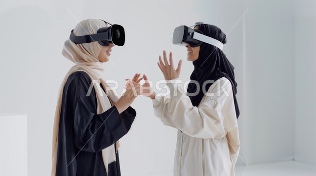 The use of modern and advanced technologies, digital transformation and technical progress, gestures of integration and focus in virtual reality, a close-up portrait of two Saudi Gulf Arab women, veiled, wearing abayas and wearing VR glasses.