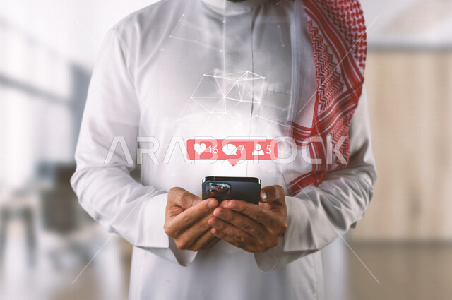 صورة مقربة لرجل عربي خليجي سعودي بين يديه جهاز أيفون ، خروج اطار قائمة الإشعارات محاطة بشبكة عنكبوتية مضيئة بتقنية الهولوجرام ، استخدام تقنية الهولوجرام ثلاثية الأبعاد .