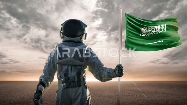 صورة مقربة لرائد فضاء عربي خليجي سعودي يحمل  بيده علم السعودية و يلبس بدلة الفضاء الخاصة ، الوصول للفضاء و القمر .