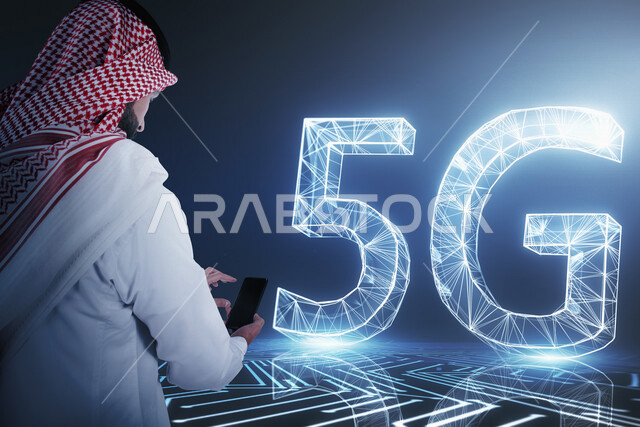 صورة مقربة من الخلف لرجل عربي خليجي سعودي بيده موبايل أمام اختصار الجيل الخامس للشبكات 5G بتقنية الهولوجرام ، استخدام خاصية الهولوجرام ثلاثية الأبعاد .
